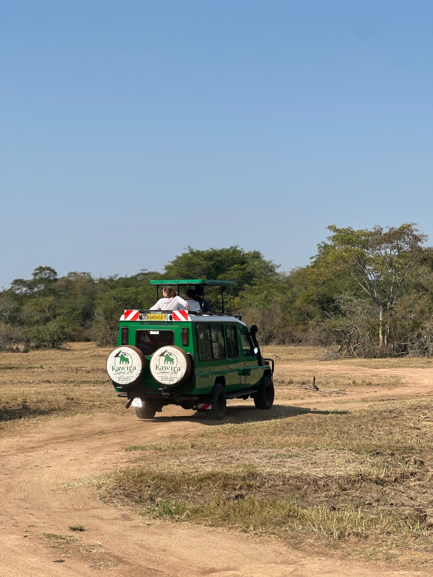 Kawira Safaris green tourist 4x4 with open roof carrying travelers across an open Akagera savanna track